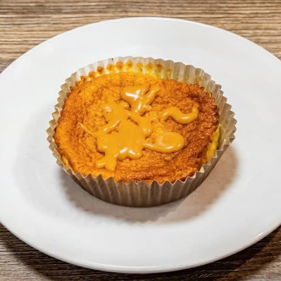 A golden-brown cupcake in a paper liner, topped with a caramel drizzle, on a white plate.