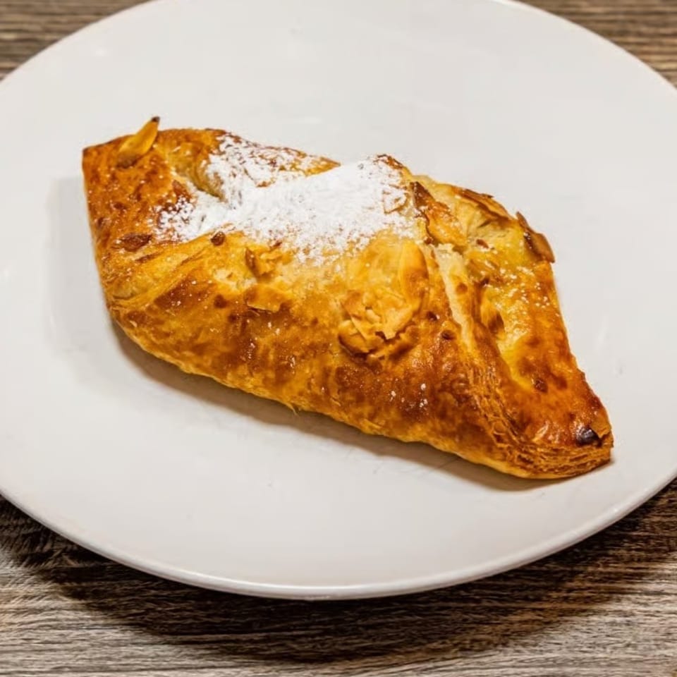 Golden brown pastry with powdered sugar and sliced almonds on a white plate.