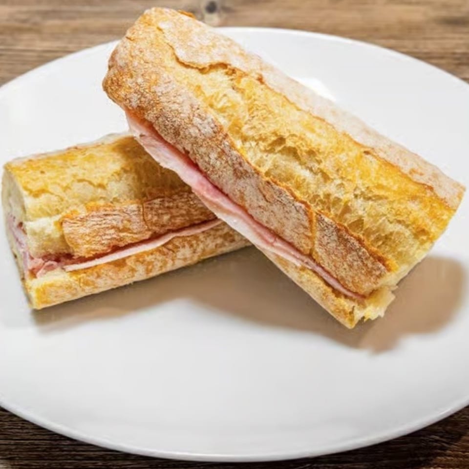 Two ham and cheese baguettes on a white plate, against a rustic wooden background.